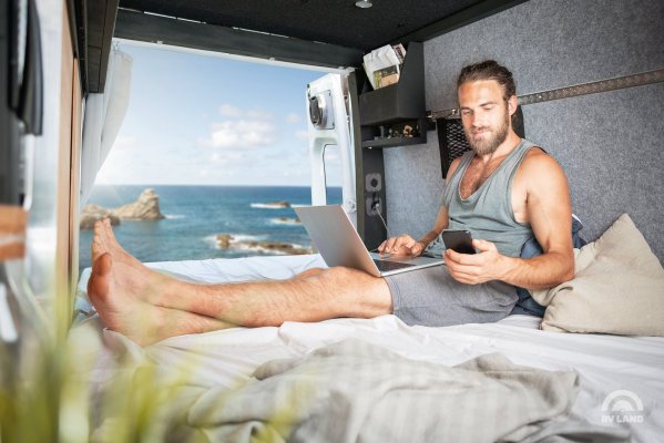 Мужчина работает с ноутбуком в кемпере на берегу моря