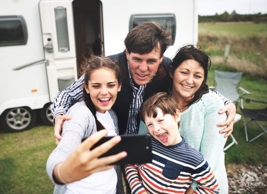 Счастливая семья делает селфи на фоне своего дома на колесах